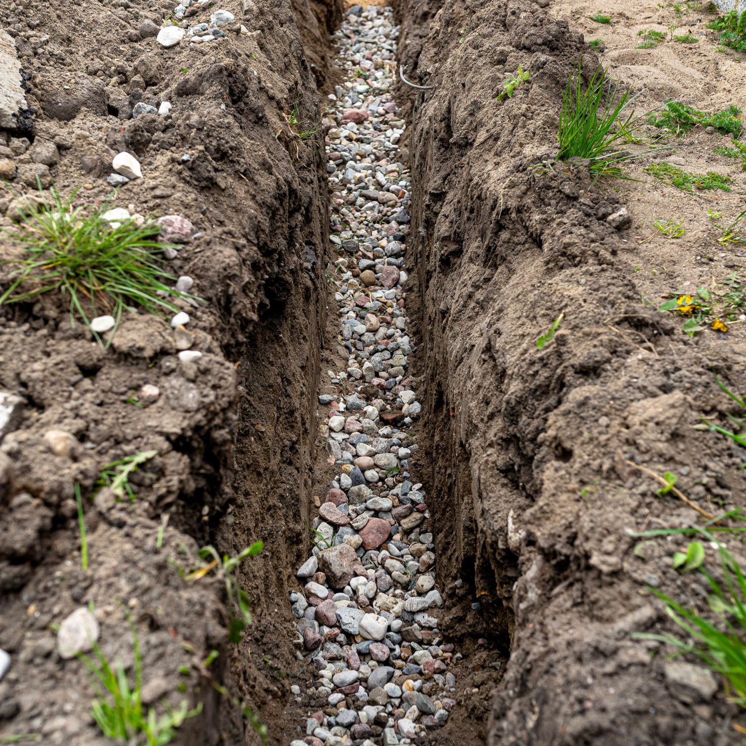 A trench dug in the yard along the fence to lay the French drain pipe.
